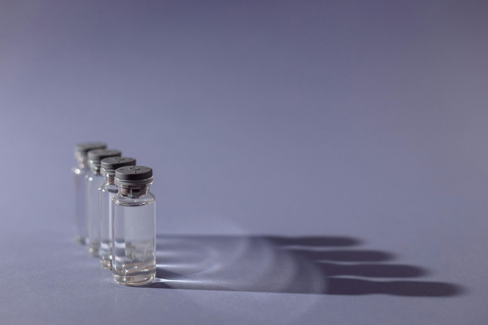Close-up of lined up vaccine vials casting shadows, symbolizing medical advancements and health.